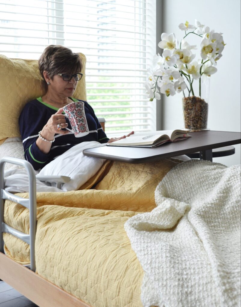 Woman reading a book on a hospital bed installed in her bedroom.